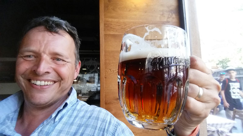 Man smiling and holding glass of dark beer in left hand