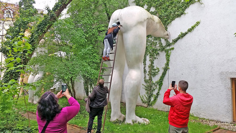 david cerny brownnosing sculpture, the marble white legs of a person bending over and a ladder to climb up to look inside the anus