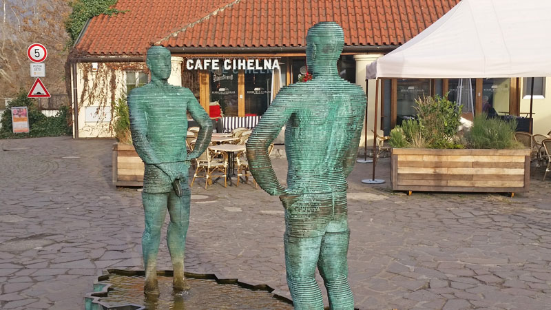 david cerny sculpture pissing men, 2 bronze sculptures standing in a pond in a courtyard