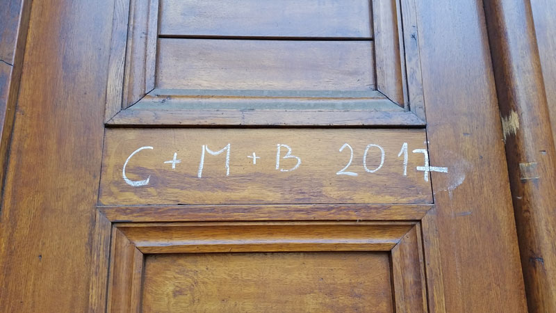 the characters C+M+B 2017 written in chalk on a wooden door