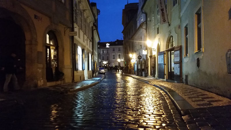 a wet cobble stone road in prague reflecting light from a street lamp