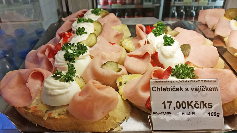 multiple ham and egg open czech sandwiches called chlebicky behind glass with sign in czech