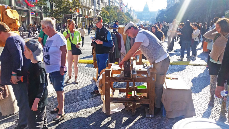 a man with a white flat cap operating a manual thredding machine at the bottom of wenceslas square. Far in the distance is the national museum