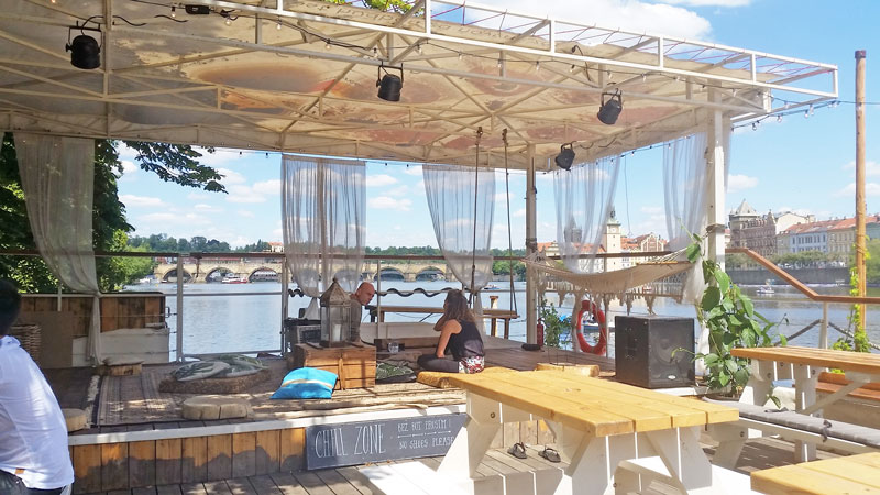 the rear of bobs bbq floating barge in prague with low seating area and see through drapes with a view of the river vltava and charles bridge