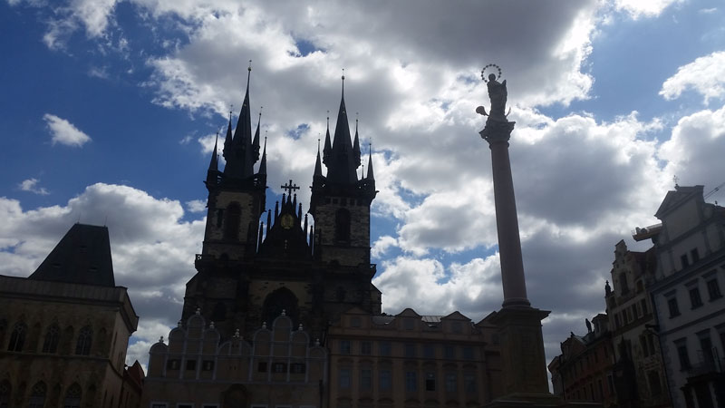 prague marian column and tyn church in silhouette against a blue sky with white clouds