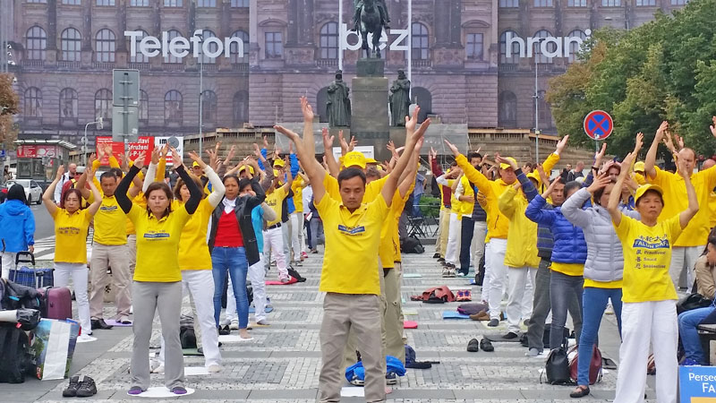 falun gong members in yellow t-shirts protest and exercise at the top of prague wenceslas square. they are standing on black and white cobbles forming concentric squares