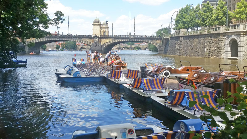 boats and prague pedalos moored on the river vltava with legion bridge in the background