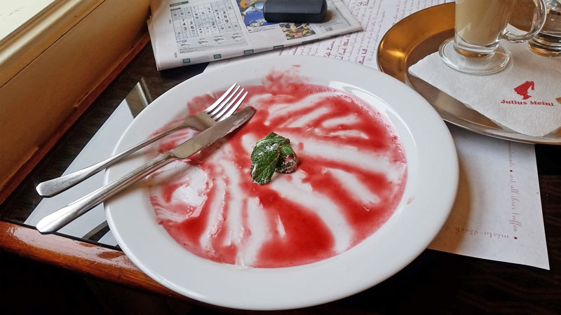 white plate with leftovers of raspberry sauce and a sprig of mint with knife and fork