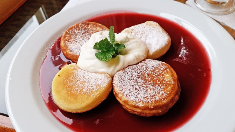 4 pieces of czech livanec pancakes on raspberry sauce and sour cream on top with a sprig of mint
