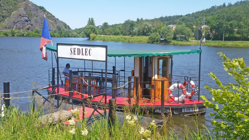 the p1 prague public transport ferry with wooden seats, a black guard rail, green roof and red deck