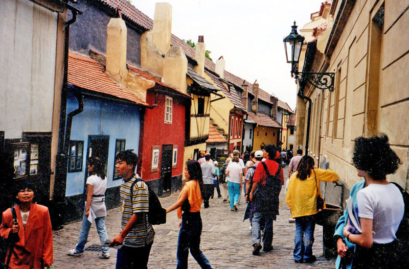 very narrow cobbled street with small houses on the left single floor and two floor brightly colured houses with chimneys