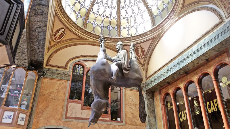 a lucerna passage sculpture of a king sitting on the belly of an upside-down horse which has it's feet tied and is hanging from the ceiling.