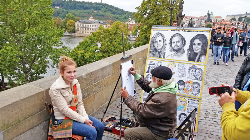 prague charles bridge portrait artist drawing a caricature of a young girl with ginger hair