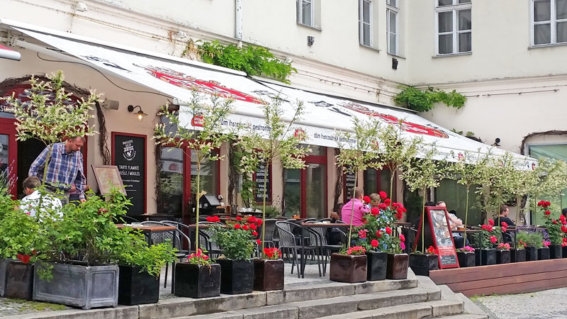 street side garden cafe called la gare in prague with stella artois awnings and potted trees