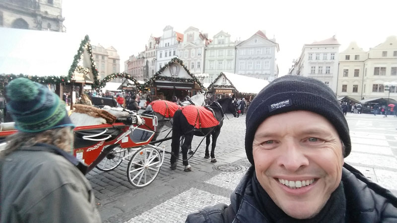 man with a black hat and behind is a horse and carriage in a prague christmas market