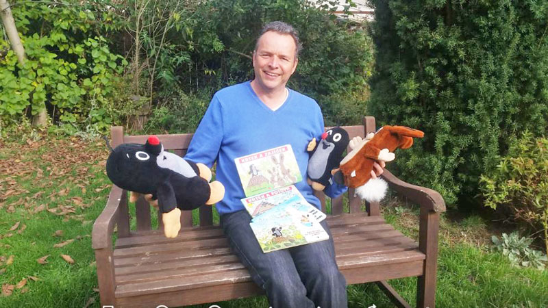 man sitting on bench with cuddly toy moles, rabbit and little mole books for kids