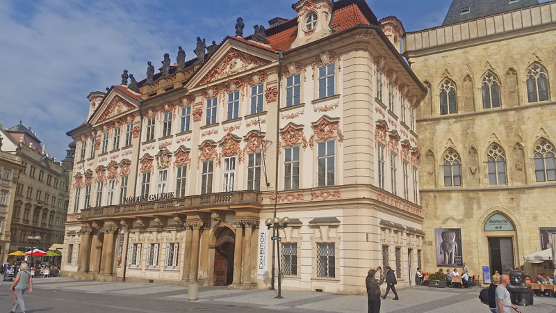 prague old town square late baroque style kinsky palace, a four floor building with stone archways joined by a first floor balcony and 2 roof level porticos