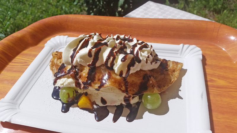 czech style folded pancake with cream and chocolate, two grapes and some peach served on a paper plate