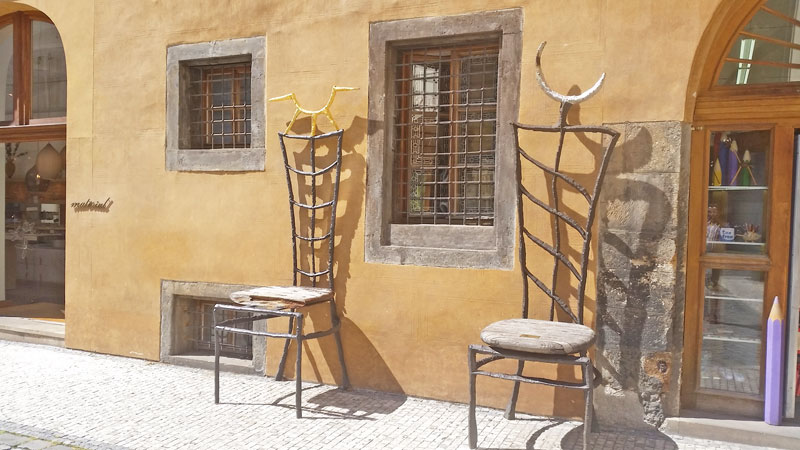 oversized artistic chairs leaning against a stuccoed gothic building in the prague tyn courtyard