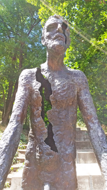 a bronze statue with a gash from the right shoulder to the waist part of the monument to victims of communism in prague