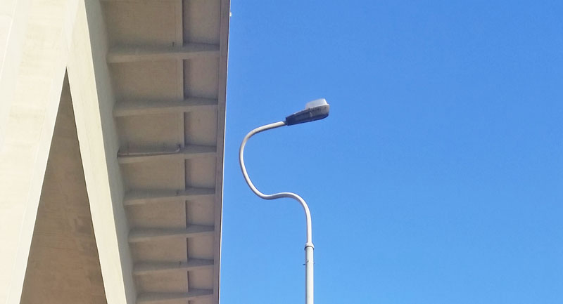 a street lamp pointing up towards a bridge with blue sky