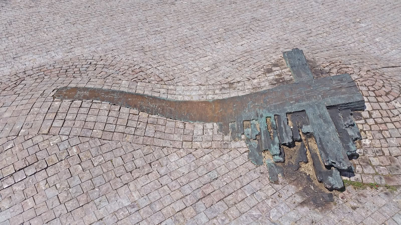 a bronze cross that appears to be burned embedded in a cobbled pavement