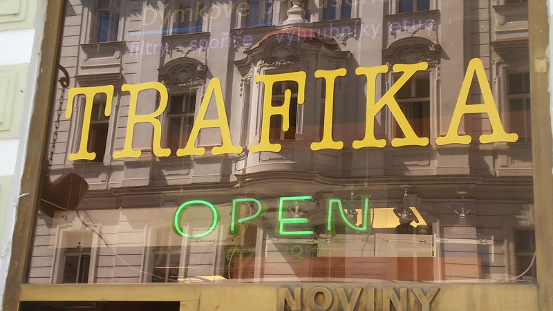 a yellow trafika or tabak sign in a shop window with the reflection of the building opposite