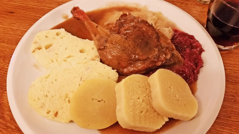 Prague Roast Duck and Dumplings with red and white cabbage and gravy on a white plate