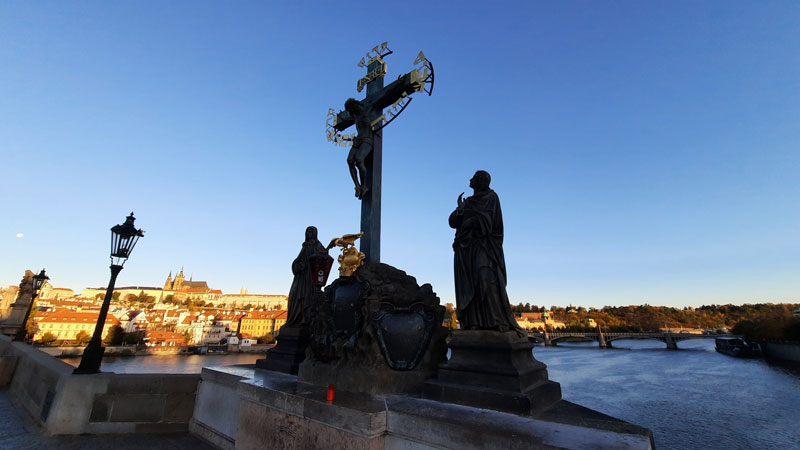 prague calvary in silhouette on charles bridge with prague castle in sunlight in the distance