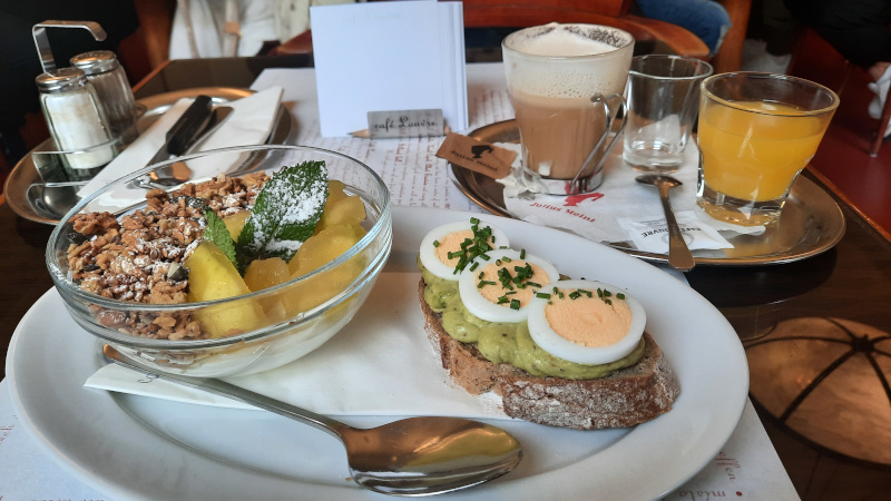 prague cafe louvre plate with avocado toast, boiled egg, juice, water and granola with yoghurt and fruit