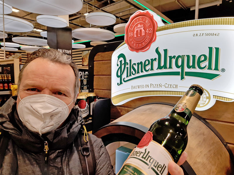man holding a bottle of pilsner urquell czech beer with logo sign behind