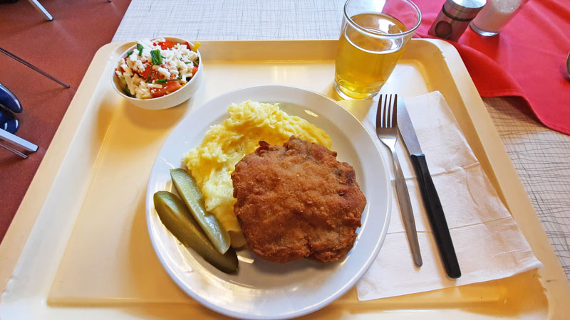 A tray with a main meal of fried karbanatek, puree potato and gherkin with a side salad and drink