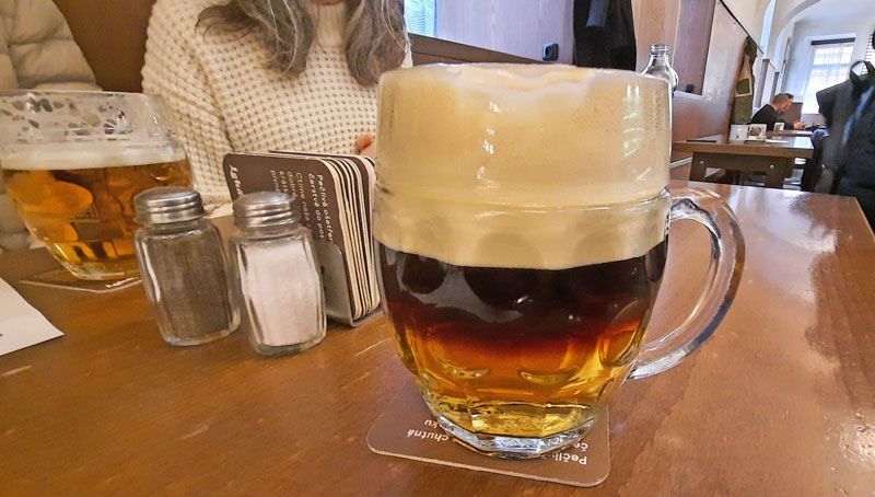 a glass of beer with a lot of foam, dark beer at the top and light beer at the bottom of the glass