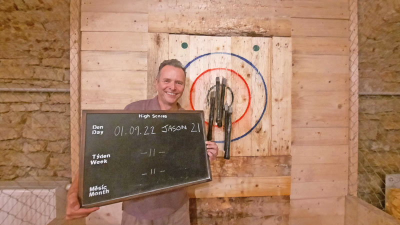 man standing in front of a target with five throwing axes stuck in it