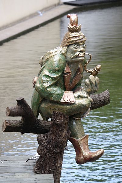 czech superstitious character called a vodnik dressed in a green jacket with gold hat and boots smoking a pipe