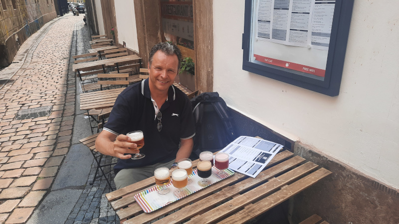 man sitting at a table holding a glass of beer from a flight of beer