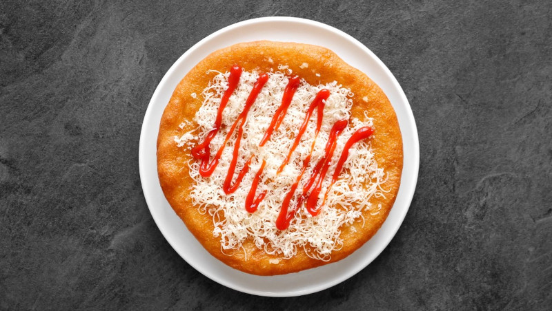 langoš with grated cheese and ketchup on a white plate