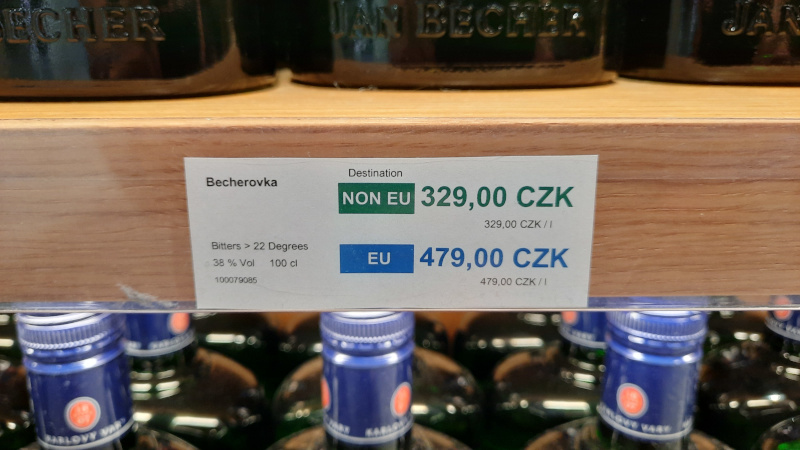 signage at a prague airport duty free shop showing EU and non-EU pricing for a 1L bottle of Becherovka