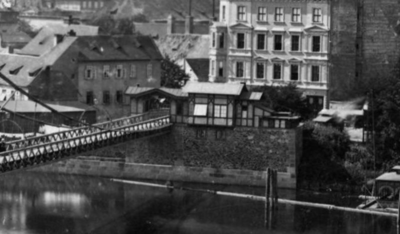 1869 picture of a timber framed building on the riverside in prague which acted as an iron footbridge toll booth