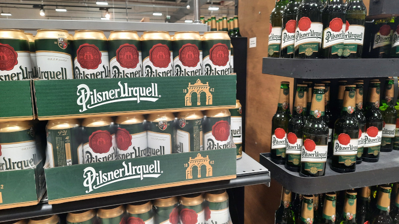bottles and tins of pilsner urquell on a supermarket shelf